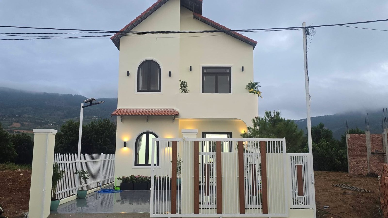 Mặt tiền nhà 2 tầng mới Đông Thanh Nam Ban lên đèn buổi tối, mái ngói đỏ, cửa vòm, view đồi núi